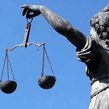 Justitia mit Wage in der Hand von schräg hinten vor blauem Himmel